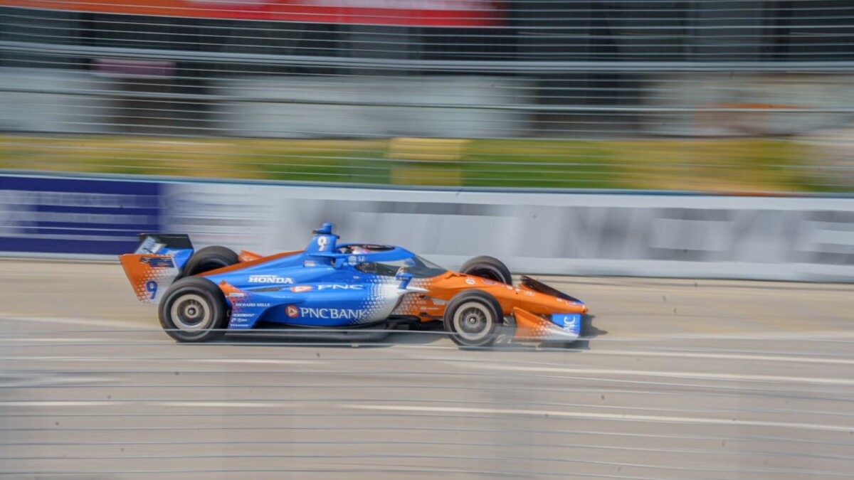 blue and orange IndyCar speeds down racetrack